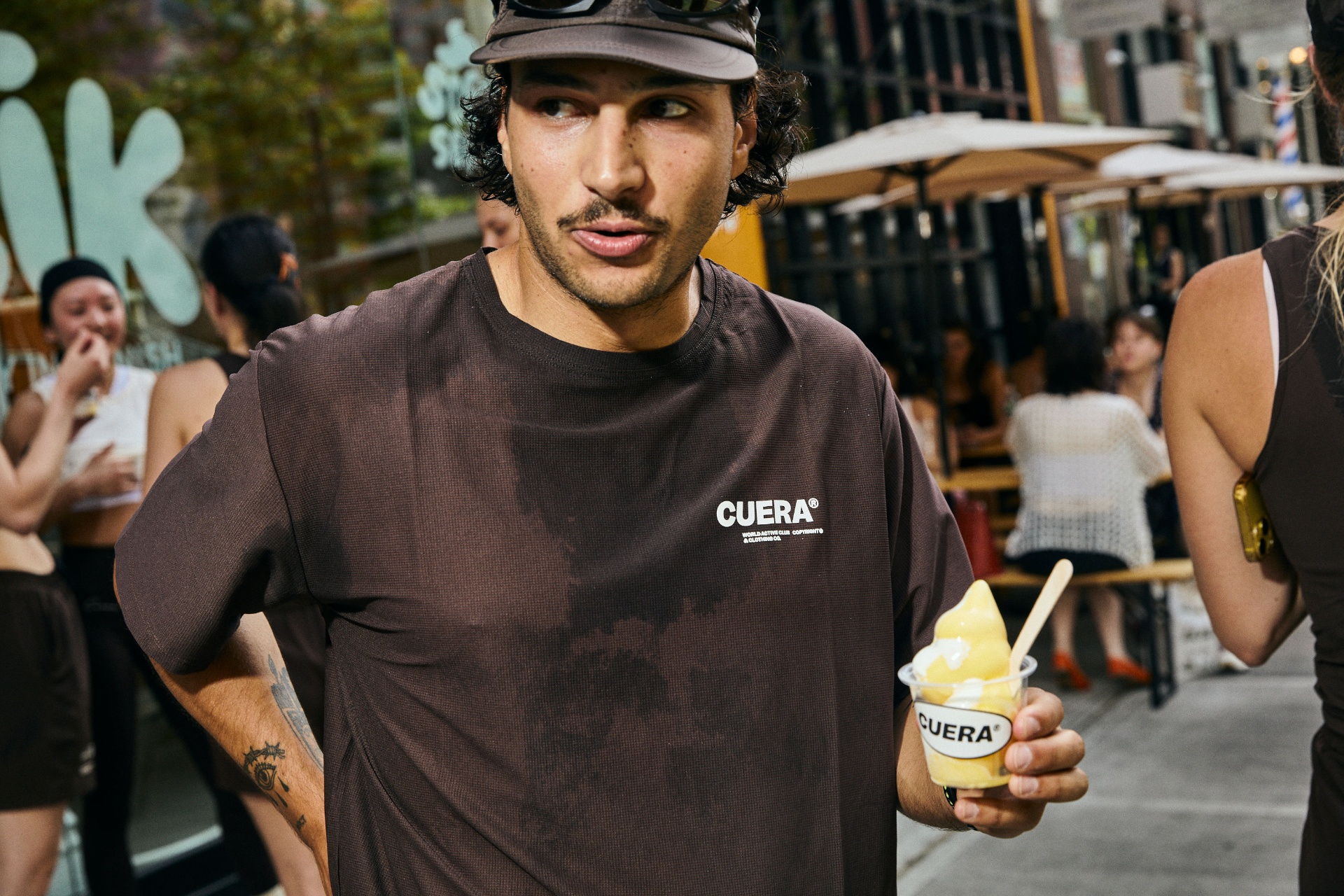 A SLIK guest in a brown CUERA tee holding a cup of SLIK soft-serve on a city street